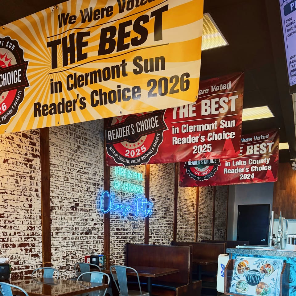 Restaurant dining area decorated with Reader’s Choice award banners, neon signage, booths, tables, and a pizza menu board.