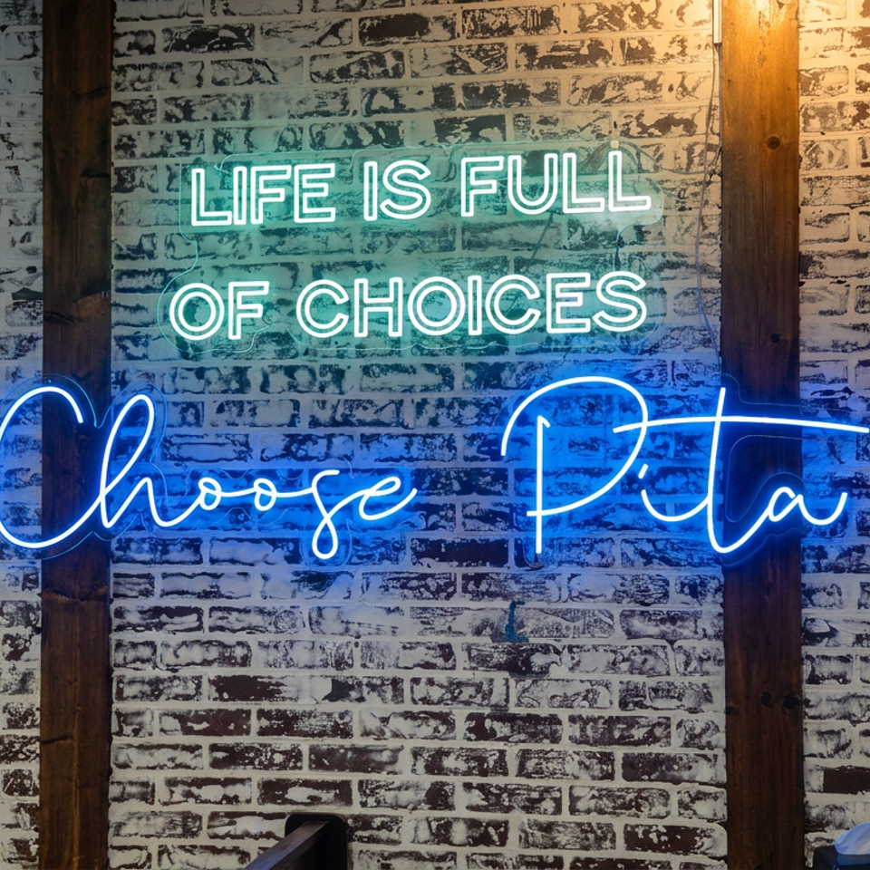 Blue neon “Choose Pita” sign reading “Life Is Full of Choices” against a white brick restaurant wall.