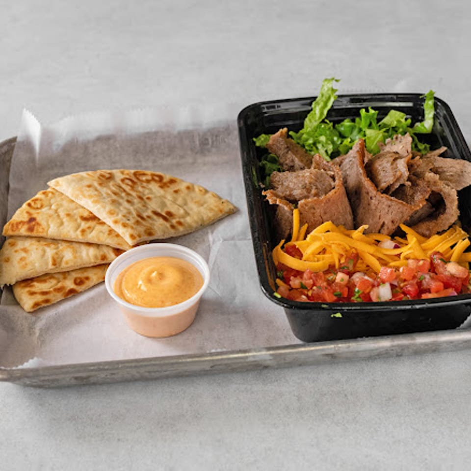 Tray with toasted quesadilla wedges, creamy dipping sauce, sliced beef, lettuce, peppers, and pico de gallo in a black container.